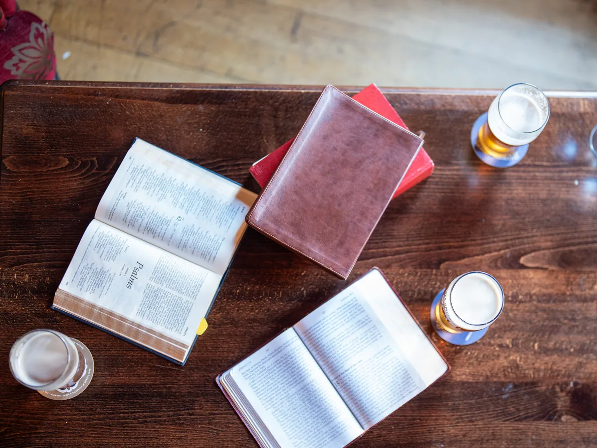 An overhead view of open books and stacked volumes on a wooden pub table.